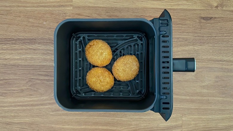 Three lobster cakes in black air fryer basket
