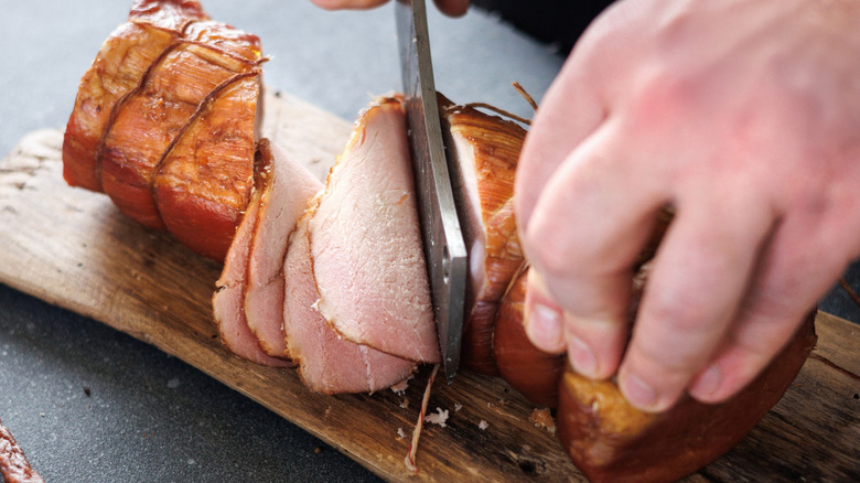 Butcher's hands slicing roast pork joint