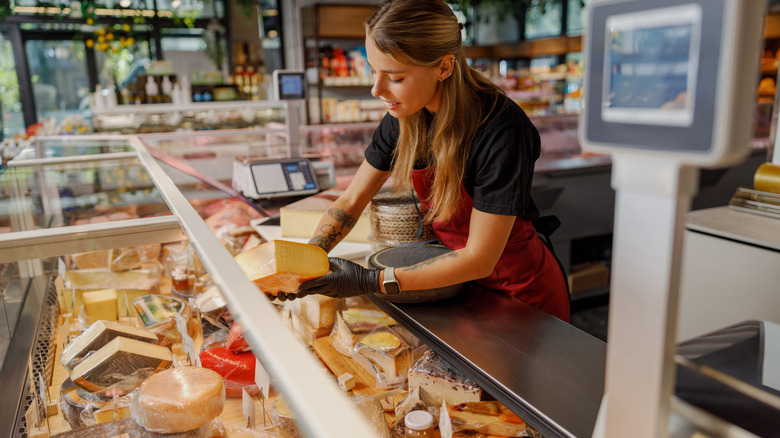 Deli employee handling cheese behind a deli counter
