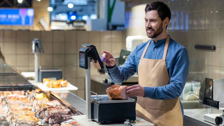 Deli clerk weighing piece of ham on scales, with equipment in the background