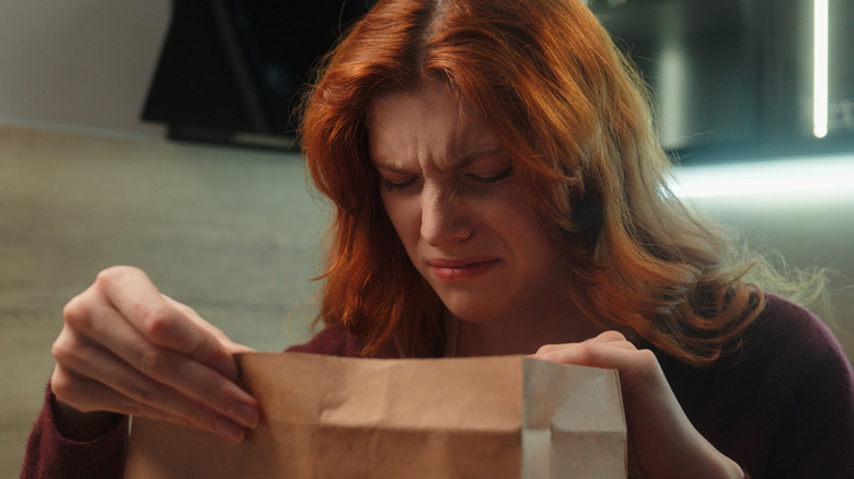 Woman wrinkling nose as she looks into a paper bag