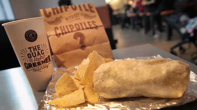 Chipotle burrito and chips with a cup and paper bag