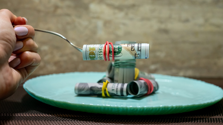 A restaurant plate with rolls of money, with one being held up on a fork