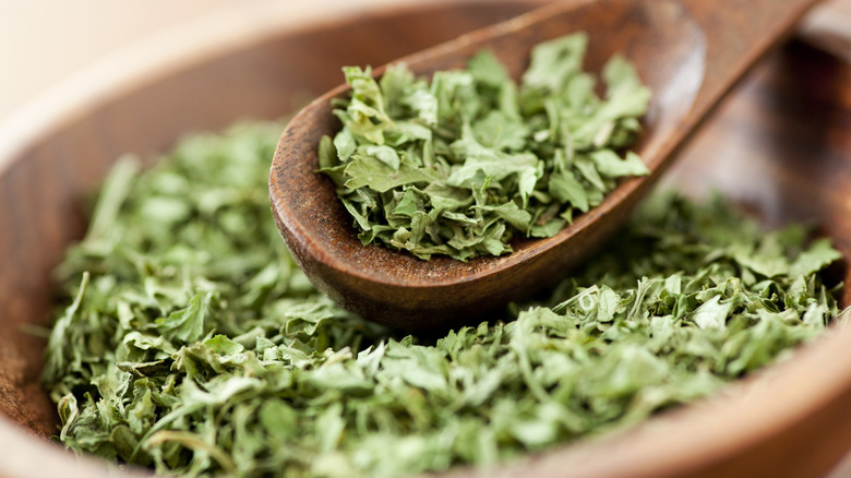 Dried parsley flakes in wooden spoon and bowl