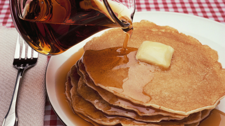 Stack of pancakes, with pat of butter on top and syrup being poured onto them
