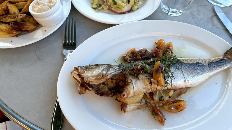 Freshly grilled fish sits on a white plate in an outdoor restaurant setting