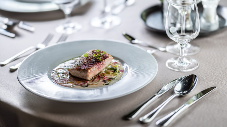 A baked salmon dish sits on a plate in a fancy restaurant