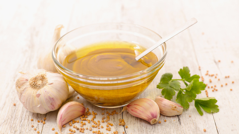 Bowl of vinaigrette, with garlic, herbs, and mustard seeds surrounding it