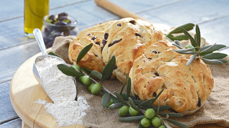 Olive bread on wooden table, with flour and fresh olives