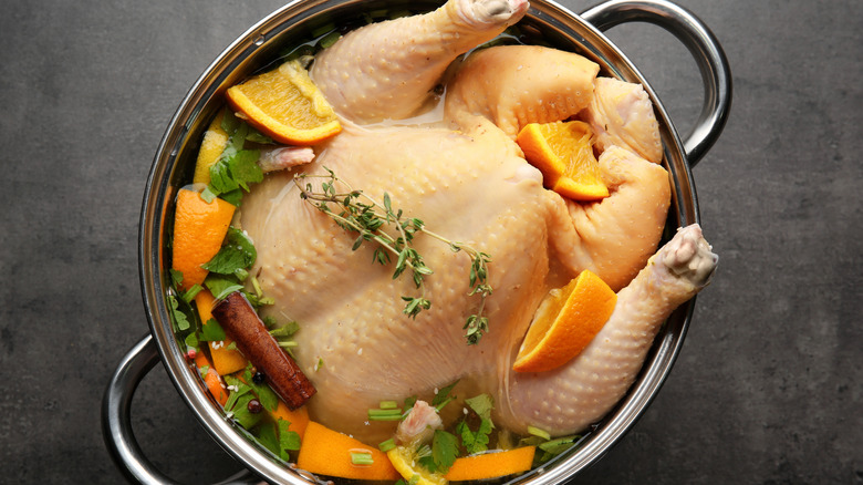 A turkey brining in a cooking pot, with spices, herbs, and slices of orange