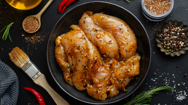 Raw marinated chicken, surrounded by spices and utensils