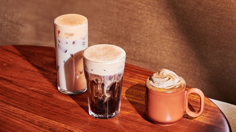 Starbucks' iced pumpkin cream chai tea latte, pumpkin cream cold brew, and pumpkin spice latte on a wood table