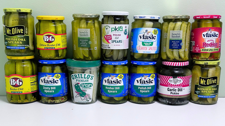 Several jars of dill pickles lined up against a green and white background