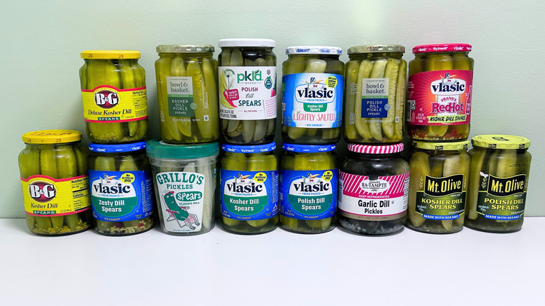 Several jars of dill pickles lined up against a green and white background