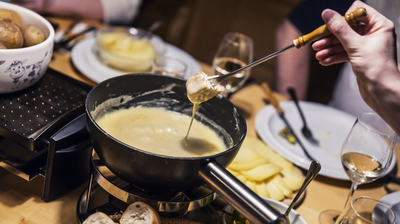 Someone dipping bread into melted cheese at a fondue party