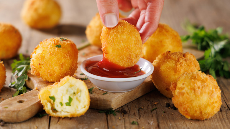 Arancini rice balls, with one being dipped into tomato sauce