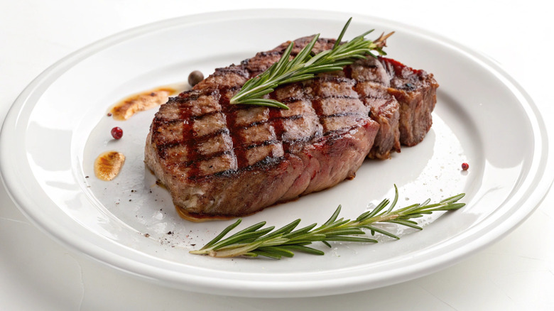 Steak with char marks and sprigs of herbs isolated on a white plate