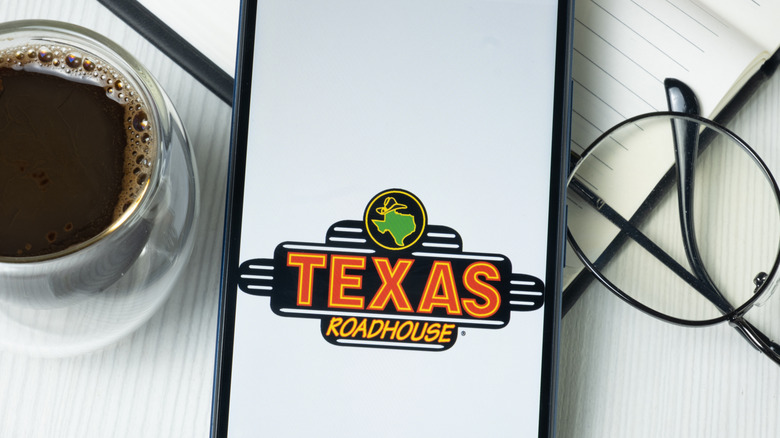 Texas Roadhouse words on  cell phone next to coffee and glasses