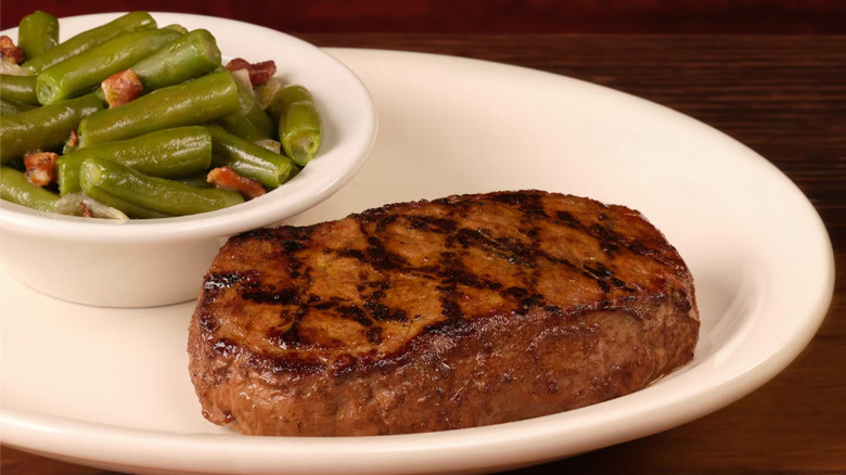 Steak and green beans sit on a white plate
