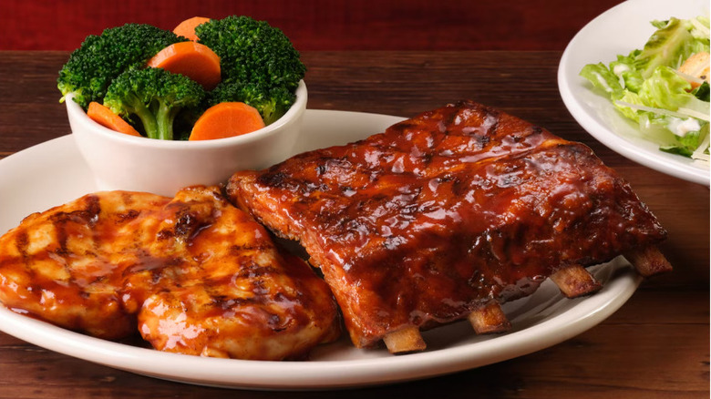 BBQ chicken and pork ribs sit on a plate with mixed vegetables next to a salad