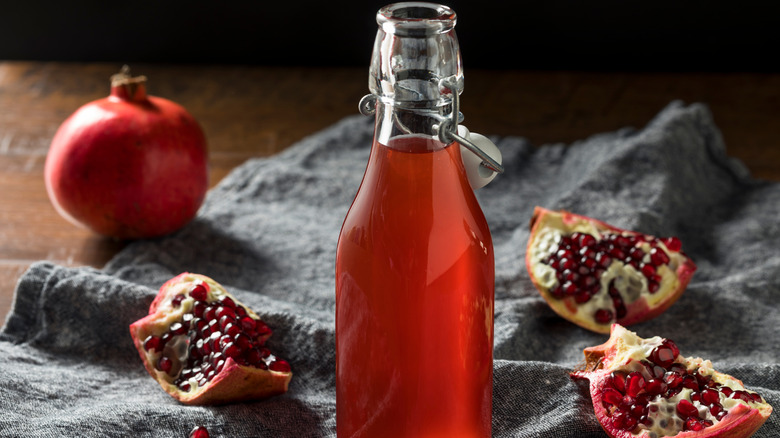 Homemade grenadine syrup in a bottle, surrounded by chunks of pomegranate