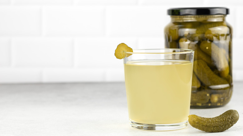 Glass of pickle juice sitting in front of a jar of pickles
