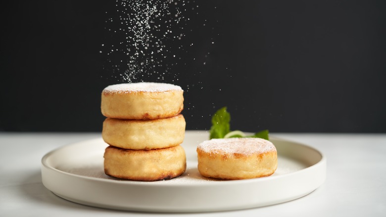 A plate of sirniki, with sugar being dusted on top of them