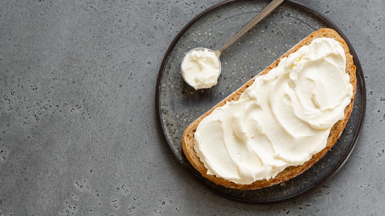A piece of toast covered in ricotta cheese, with a spoonful of ricotta cheese next to it