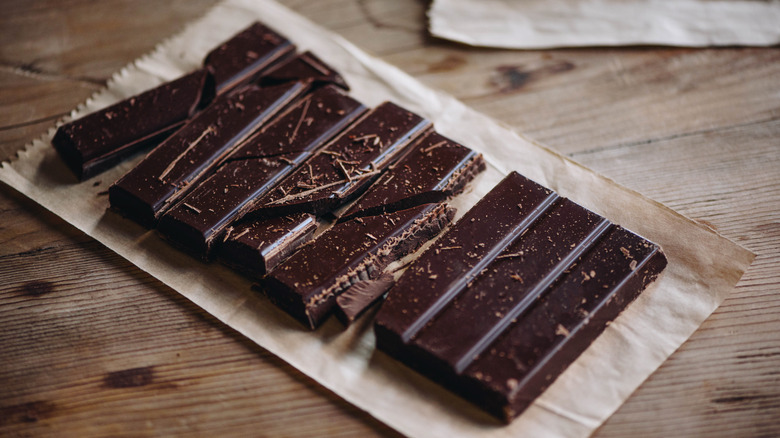 A broken bar of dark chocolate sits on a paper bag