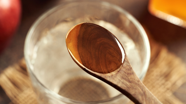 Apple cider vinegar in spoon over a bowl of water