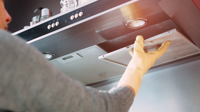 A person removes a filter from a range hood