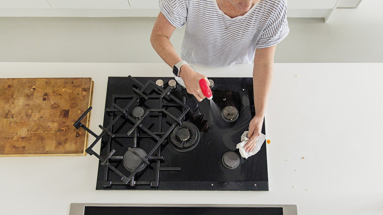Overhead view of a person cleaning a stovetop with a spray bottle and a cloth