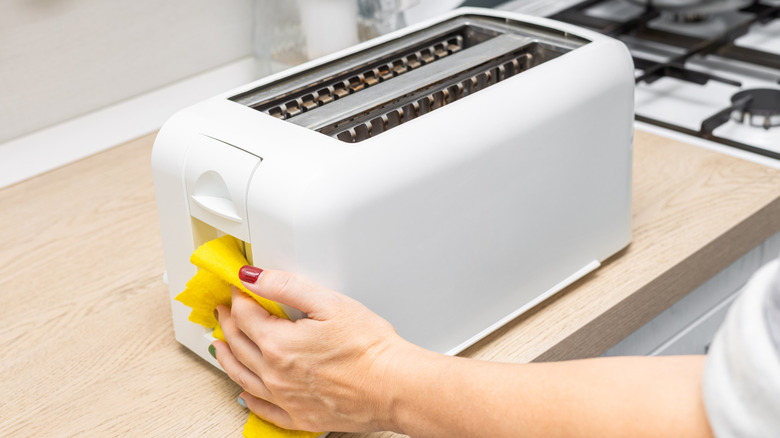 A person wipes a toaster with a yellow cloth