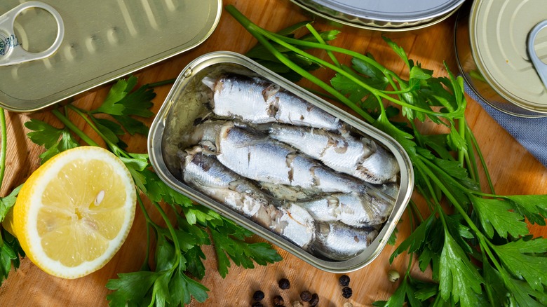 canned sardines surrounded by herbs