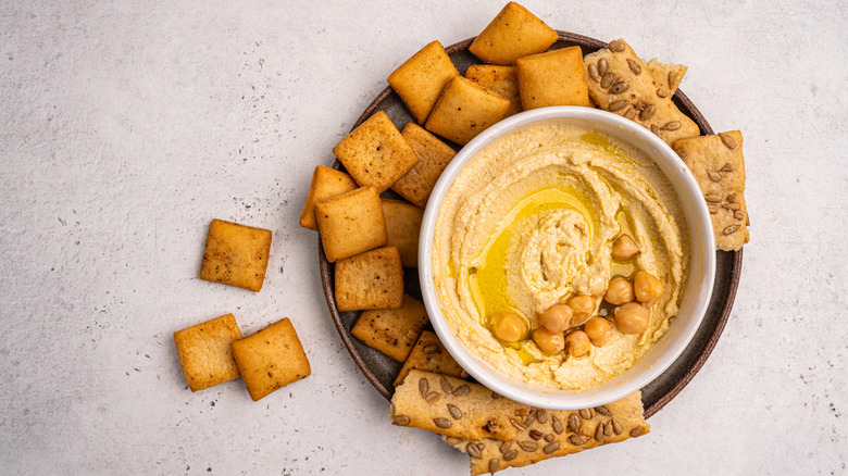 A bowl of hummus topped with olive oil and chickpeas, surrounded by crackers