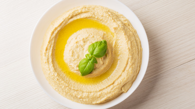 Bowl of hummus, topped with olive oil and basil leaves