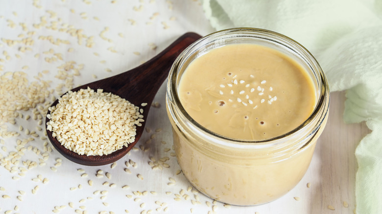 Bowl of tahini, topped with sesame seeds, with a spoon of sesame seeds next to it