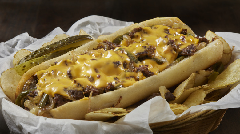 Philly cheesesteak, with chips with pickles, in a basket