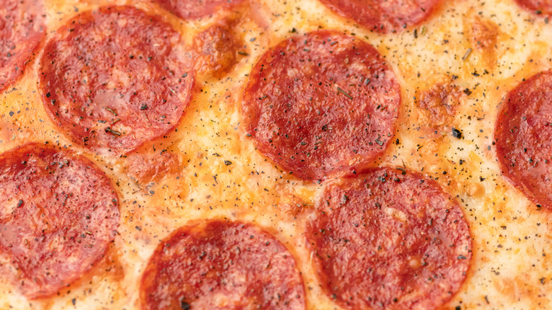 Close up of pepperoni and melty cheese seasoned with black pepper and herbs