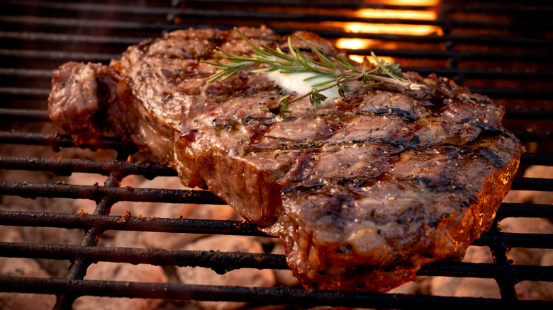 Juicy ribeye steak on a grill with fresh herbs