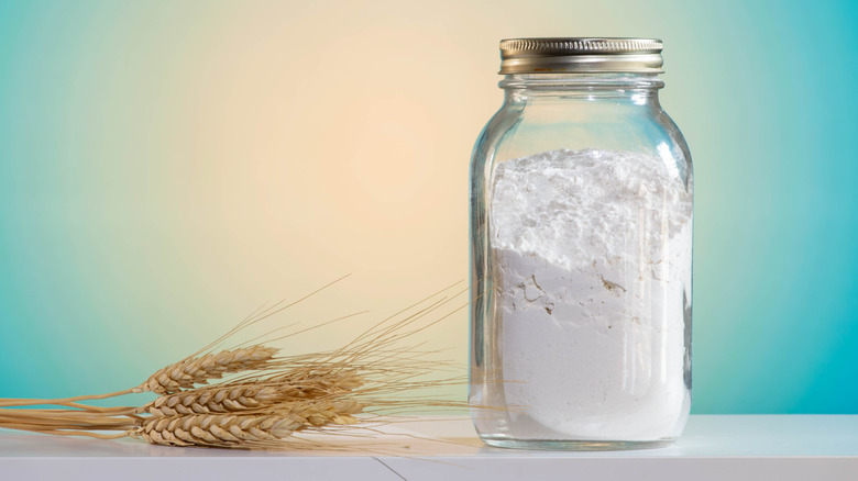 White flour in mason jar, with a wheat sheaf next to it