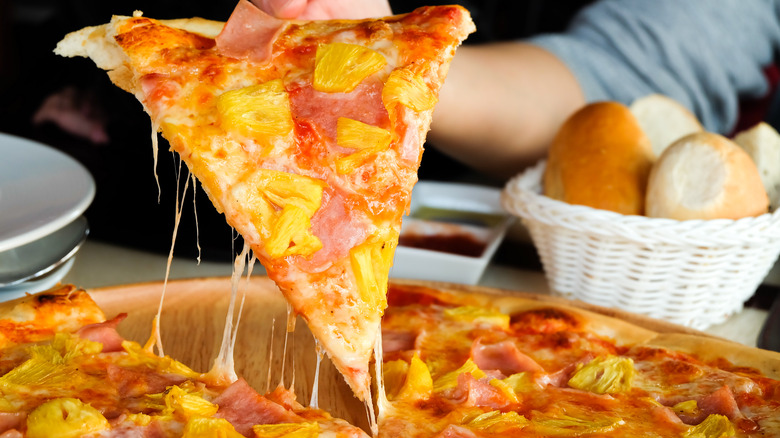 Hand grabs Hawaiian pizza slice