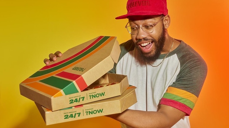 Happy man holding a stack of 7-Eleven pizza boxes and peaking inside one