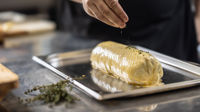 A chef sprinkles puff pastry with dried thyme for beef Wellington