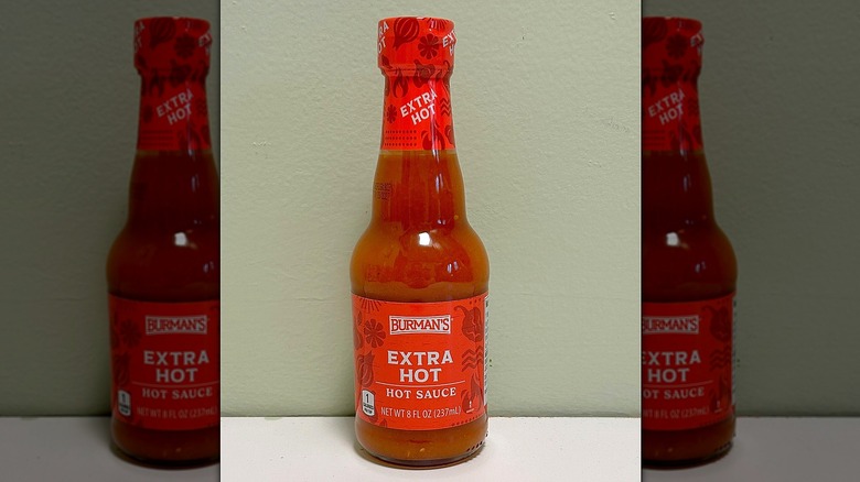 A bottle of Burman's Hot Sauce on a green and white background