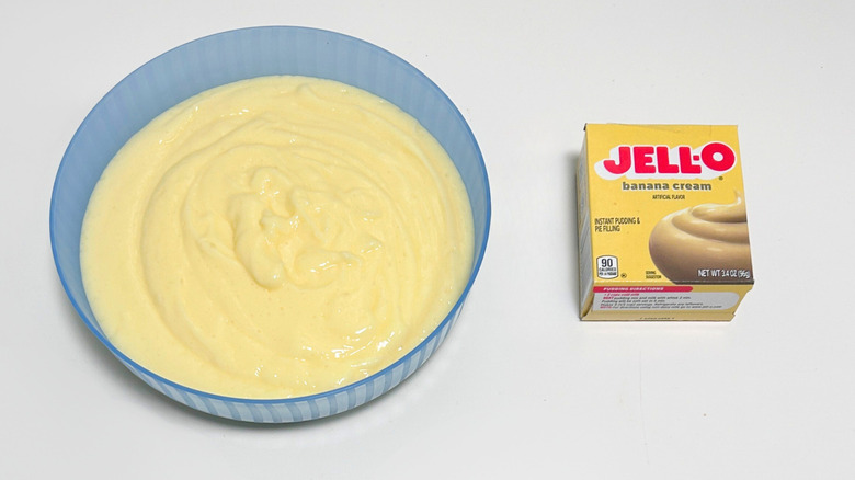 A bowl of light yellow pudding next to a box of Jell-O Banana Cream Pudding Mix