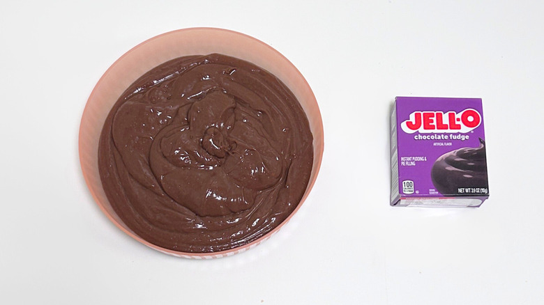 A bowl of chocolate brown pudding next to a box of Jell-O Chocolate Fudge