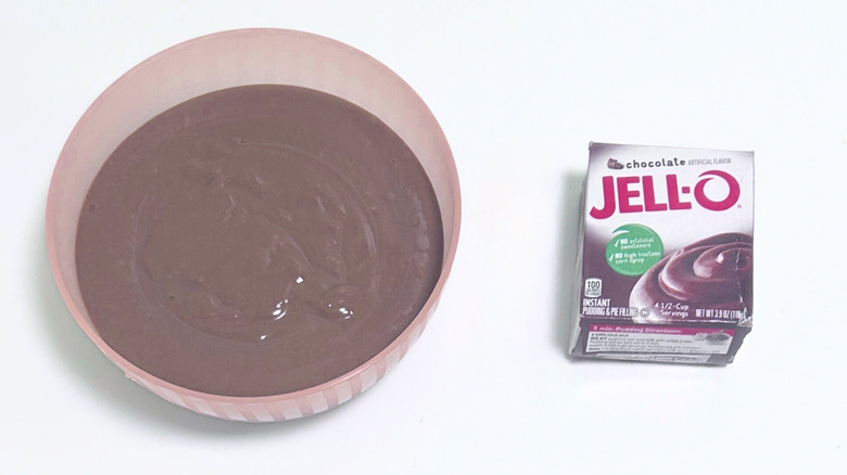 A bowl of milky brown pudding next to a box of Jell-O Chocolate Pudding Mix