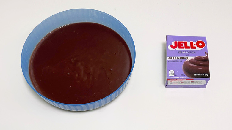 A bowl of dark brown pudding next to a box of Jell-O Cook and Serve Chocolate Pudding Mix