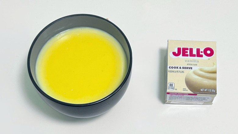 A bowl of pudding with a bright yellow skin on top, next to a box of Jell-O Cook and Serve Vanilla Pudding Mix